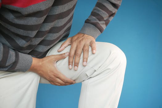 Close-up of a man's hands on his knee, showing pain or injury, on a blue background.